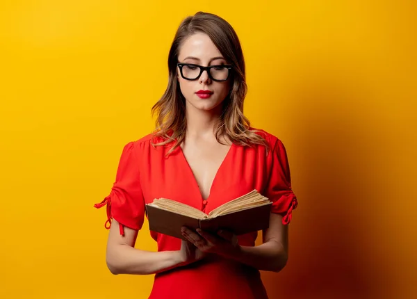 Mulher bonita em vestido vermelho com livro sobre fundo amarelo — Fotografia de Stock