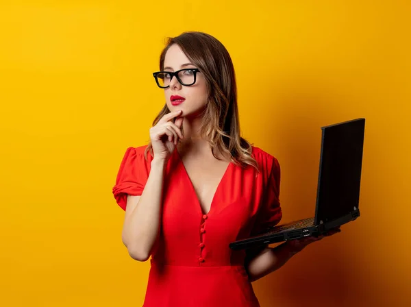 Bella donna in abito rosso con computer portatile su retro giallo — Foto Stock