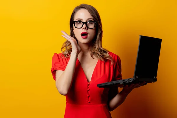 Mulher bonita em vestido vermelho com computador portátil na parte traseira amarela — Fotografia de Stock