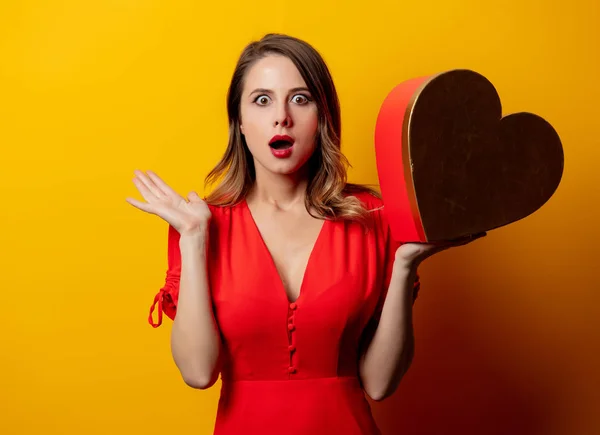 Mulher bonita com caixa de forma de coração no fundo amarelo — Fotografia de Stock