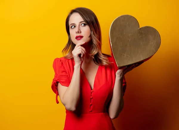 Beautiful woman with heart shape box on yellow background — Stock Photo, Image