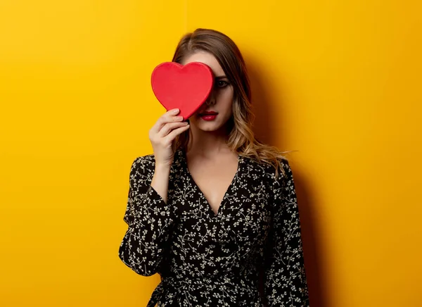 Beautiful woman with heart shape box on yellow background — Stock Photo, Image