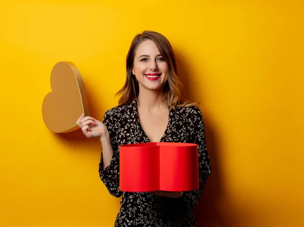 Mulher bonita com caixa de forma de coração no fundo amarelo — Fotografia de Stock