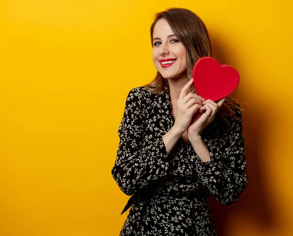 Hermosa mujer con caja de forma de corazón sobre fondo amarillo —  Fotos de Stock