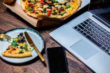 Kartonda zeytin ve peynirli Akdeniz pizzası. Tahta masadaki dizüstü bilgisayarın yanında.