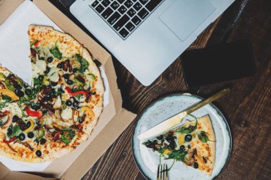 Kartonda zeytin ve peynirli Akdeniz pizzası. Tahta masadaki dizüstü bilgisayarın yanında.