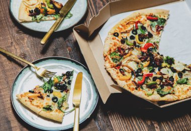 Kartonda zeytin ve peynirli Akdeniz pizzası ve masada bir tabakta