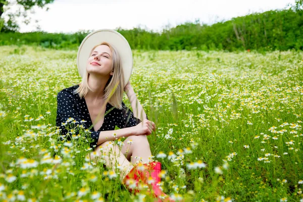 ブロンド女性で黒ドレスで田舎のシャモアの花のフィールドに座って — ストック写真