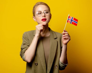 Sarı arka planda Norveç bayrağı olan ceketli şık sarışın kadın.