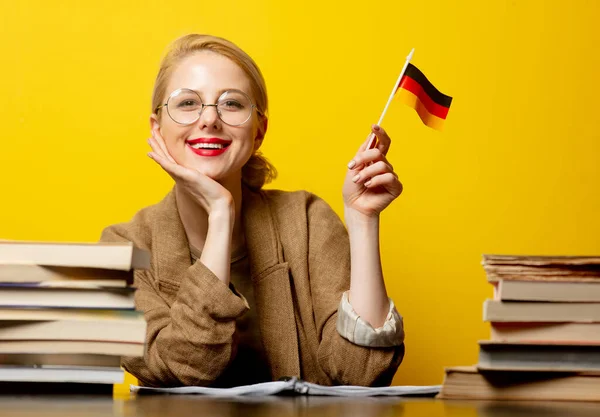 风格金发碧眼的女人坐在桌旁 背负着黄底的德国书籍和国旗 — 图库照片