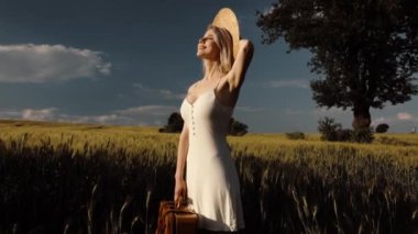 Bavullu sarışın kadının yaz mevsiminde buğday tarlasında çekilmiş videosu.