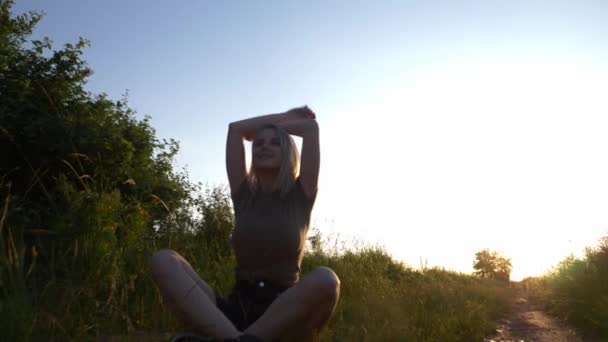ブロンドの女性は日没時に田舎道に座っている — ストック動画