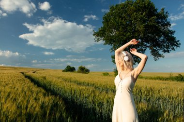 Buğday tarlasında dans eden kulaklıklı sarışın kadın.