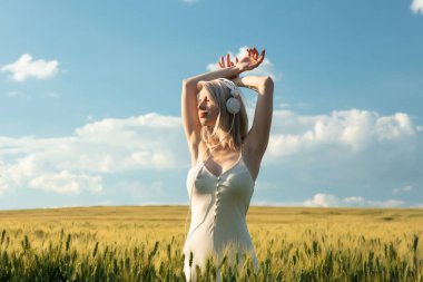 Buğday tarlasında dans eden kulaklıklı sarışın kadın.