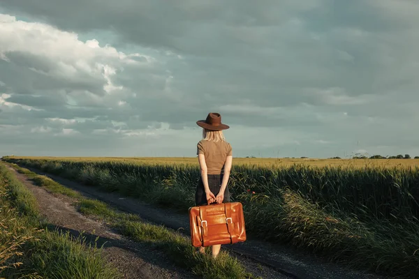 美しいですブロンド女の子とともにスーツケースで田舎道で日没時間 — ストック写真