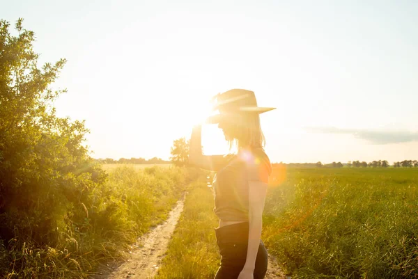日落时 戴着帽子的漂亮金发姑娘在乡间路上 — 图库照片