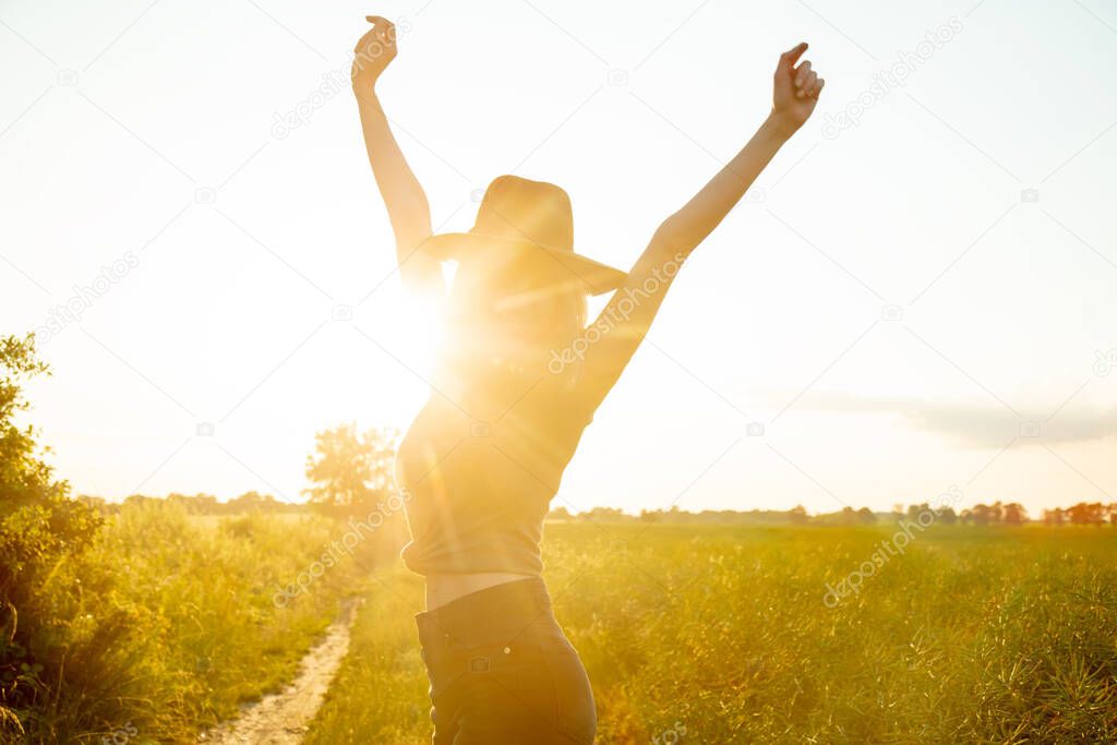 beautiful blonde girl in hat is in countryside road during sunset