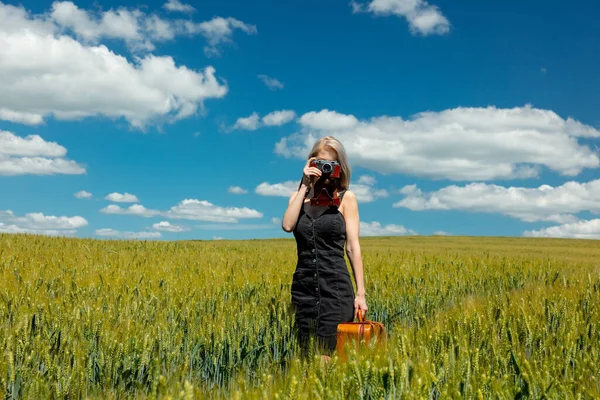 美しいですブロンド女の子とともにスーツケースとヴィンテージカメラで小麦畑で晴れた日 — ストック写真