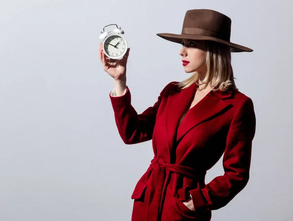 グレーの背景に目覚まし時計と赤いコートとヴィンテージの帽子のブロンドの女の子 ノアスタイルの画像 — ストック写真