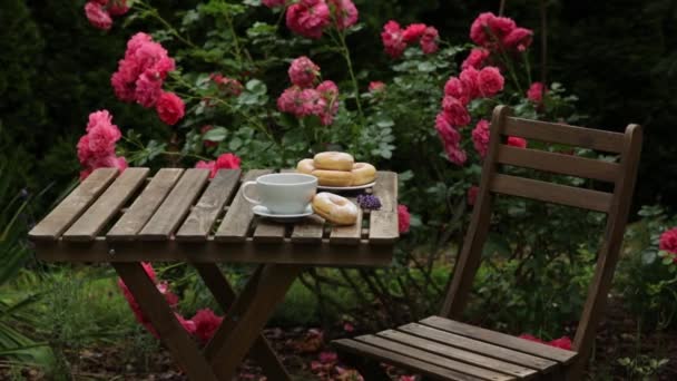 庭の木のテーブルの上でコーヒーとドーナツを飲み — ストック動画