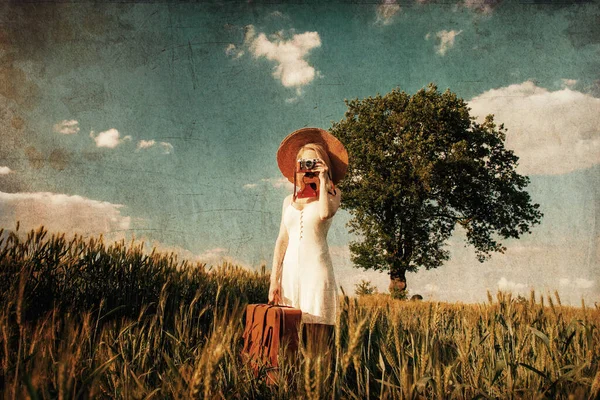Blonde woman with suitcase and camera in wheat field in summer time