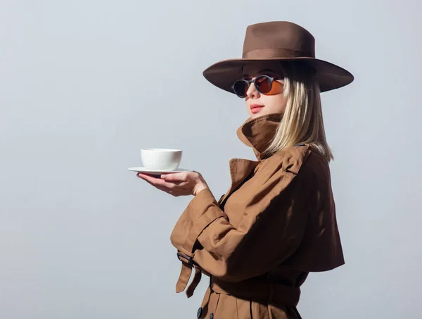 クローク サングラスのスタイルの女性は灰色の背景にコーヒーカップを保持しています — ストック写真