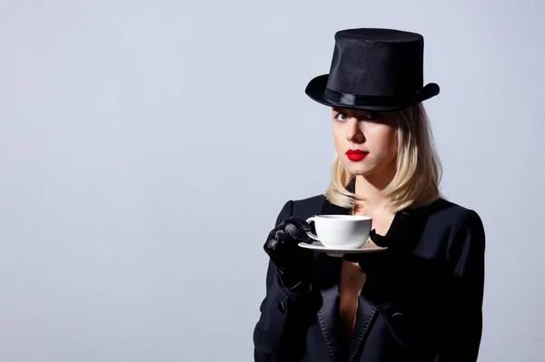 ブロンド女性で黒ジャケットとトップ帽子とともにコーヒーのカップの白の背景 — ストック写真