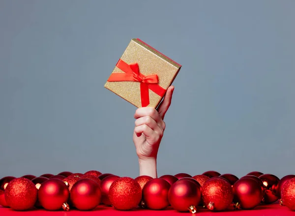 Weibliche Hand Hält Weihnachtsbox Auf Grauem Hintergrund Mit Kugeln Herum — Stockfoto