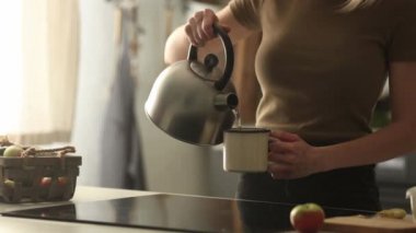 Kadın çaydanlıktan bardağa kaynar su döker.