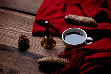 Bir fincan kahve ve ahşap masa üzerinde Noel çanı ve eşarp.