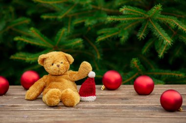 Oyuncak ayı ve Noel şapkası ahşap masanın üstünde. Arka planda ladin dalları var.