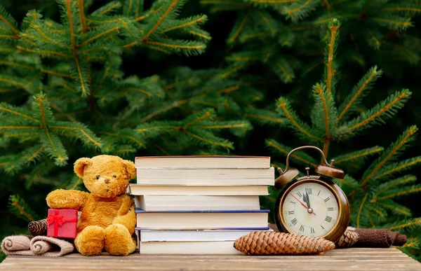 老式闹钟 玩具熊和书桌上的书籍 背景是云杉树枝 — 图库照片