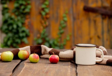 Bahçedeki ahşap masada bir fincan kahve ve elma. 