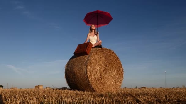 Blondes Mädchen Mit Koffer Und Regenschirm Sitzt Bei Sonnenuntergang Auf — Stockvideo