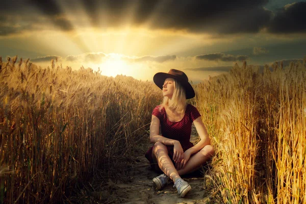 Şapkalı Kırmızı Elbiseli Sarışın Kız Buğday Tarlasında Oturuyor — Stok fotoğraf