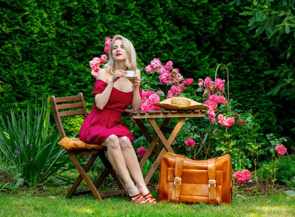 Vacker Blond Flicka Röd Klänning Med Resväska Dricker Kaffe Trädgård — Stockfoto