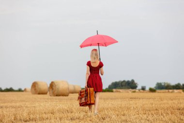 Şemsiyeli kırmızı elbiseli sarışın ve yağmurdan önce buğday tarlasında bavul.