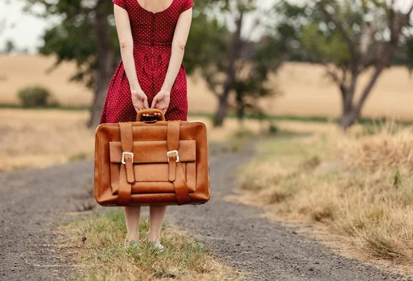 girl in red dress with a suitcase on a rural road before the rain