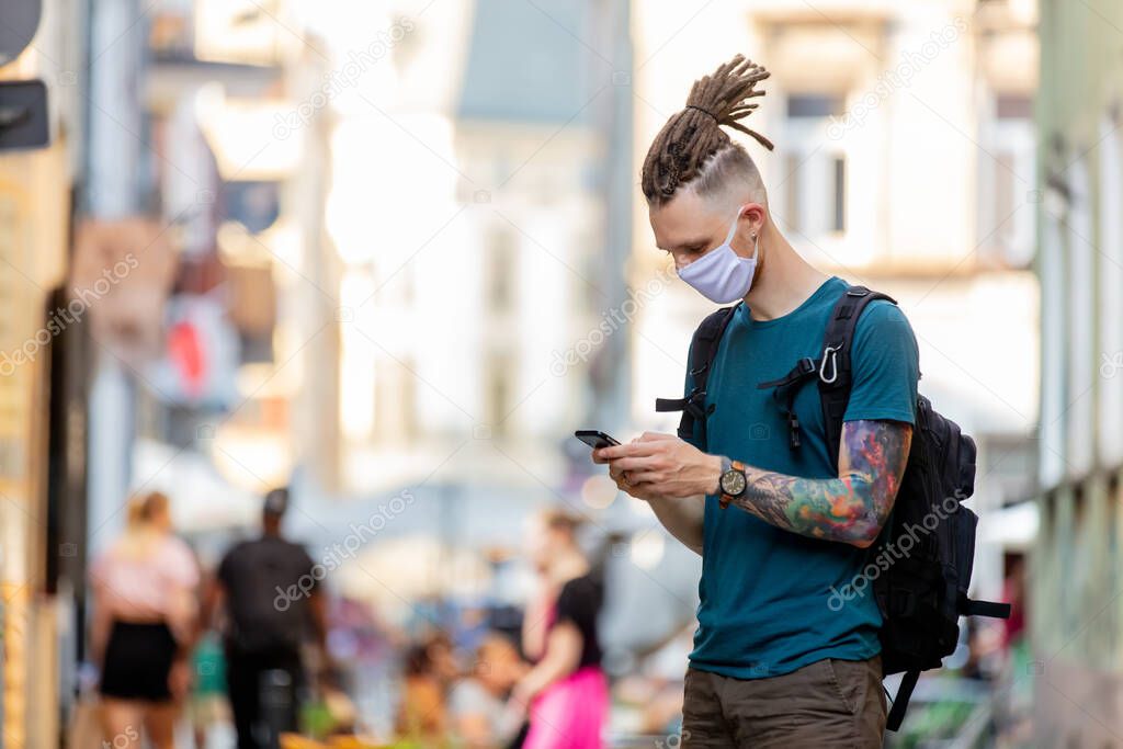 young guy with face mask and dreadlocks is using mobile phone on the street
