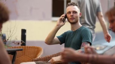 Telefonu ve kahvesi olan genç adam şehirdeki bir kafede oturuyor.