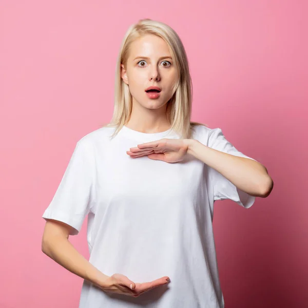 ブロンド女性でホワイトMoch Tシャツ上のピンクの背景 — ストック写真
