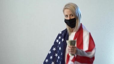 Amerika bayrağı ve beyaz arka planda parası olan maskeli sarışın kız.