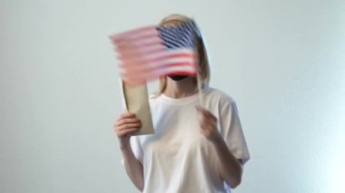 Amerika bayrağı ve beyaz arka planda parası olan maskeli sarışın kız.