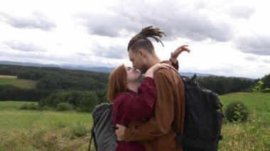 Genç çift, arka plandaki dağlara sarılıyor.