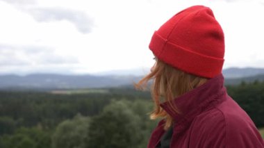 Kırmızı şapkalı genç kız dağlara bakıyor. 
