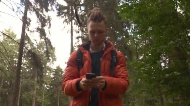 Genç adam ormanda cep telefonu kullanıyor.