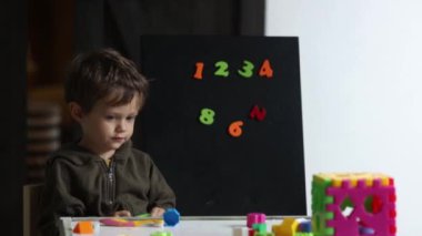 Anaokulu öğrencisi evde oyunlarla masada oturuyor. 