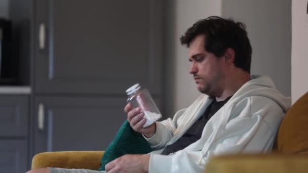 風邪をひいた男が薬を持ってソファに座り — ストック動画