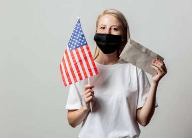 Amerika bayrağı ve beyaz arka planda parası olan maskeli sarışın kız.