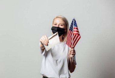 Amerika bayrağı ve beyaz arka planda parası olan maskeli sarışın kız.